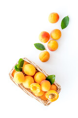 Fresh raw apricots in basket on white background top view copy space, pattern with leaves