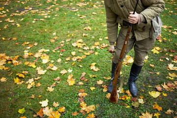 Man with rifle dressed in soviet soldier uniform of World War II hides knife behind boot top.