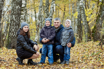 Father with daughter and two sons walks in autumn forest.