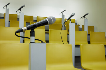 Closeup microphone in holder in auditorim with yellow chairs and microphones.