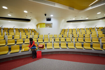 Woman sits in auditorium with yellow chairs.