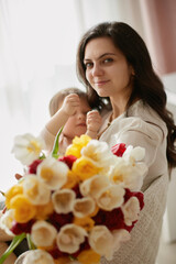 Cute little baby daughter and mom with flowers tulips. Mother and child hugging. Happy mother's day.