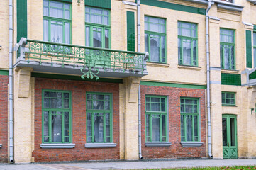 Fototapeta na wymiar The facade of an ancient building decorated with metal patterned details. The brick facade of the building has a balcony. The architecture of the last century.