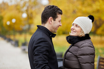 Half-length portrait of smiling man and woman in autumn park, profile view.