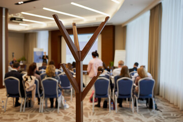 Wooden hat and coat stand in room with people sitting on chairs, shallow dof.