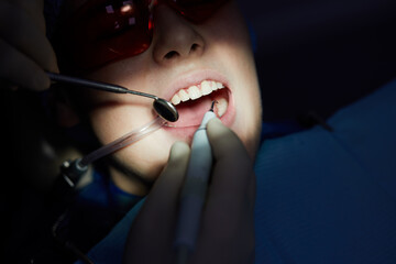 Dentist makes ultrasonic teeth cleaning to boy using special tools in dental clinic.
