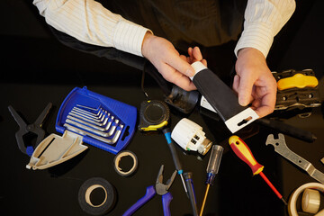 Male hands hold black tube above table with different tools.