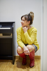 Smiling senior woman sits squatted near electric piano in room.