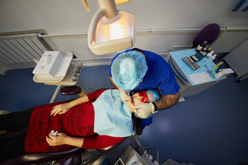Dentist works with dental instruments in mouth of female patient on dental chair.