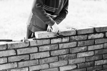 a man builds a brick wall, puts a brick on a cement-sand mortar, removing excess mortar with a...