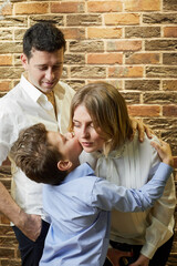 Obraz na płótnie Canvas Little boy kisses his mother in cheek, father looks on them.