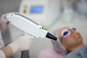 Beautician holds laser for epilating patient face, shallow dof, focus on laser.