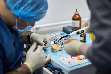 Stomatologist and assistant prepare dental implant on medical table.