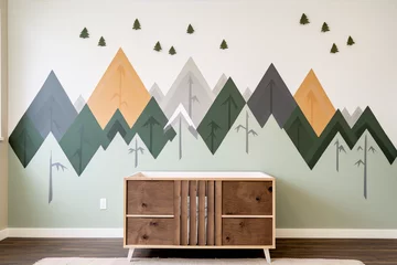 Crédence de cuisine en verre imprimé Montagnes A mural of green, gray and brown mountains and trees in a geometric style painted on a wall behind a wooden dresser.