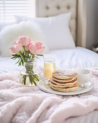 Fototapeta na wymiar Still life of a breakfast in bed with pancakes, flowers and juice in a soft pink color scheme.