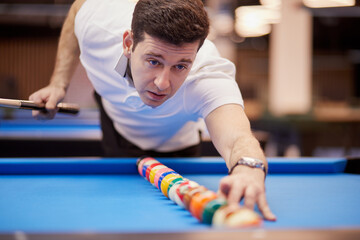 Man in white polo-neck shirt aligns balls in line on pool table.