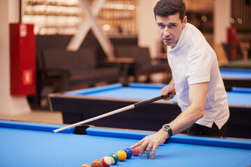 Man in white polo-neck shirt aligns balls in line on pool table in club, focus on hand.