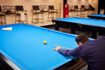 Man in dark blue shirt plays pool in club, rear side view. - Powered by Adobe