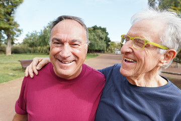 Two male senior friends having fun during workout running at city park - Happy mature men doing fitness exercise outside - Sport and eledrly healthy lifestyle concept - Main focus on left face