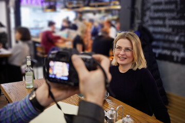 Photographer takes picture of smiling woman sitting at table in cafe.