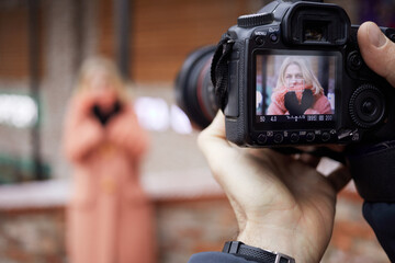 Display of camera with preview of female portrait in hands of photographer outdoor.