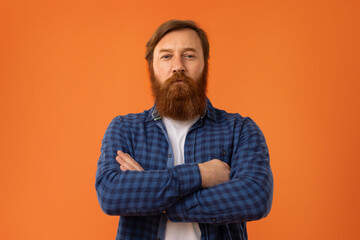 Redhaired bearded man crossing arms on chest against orange backdrop