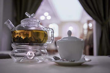 Transparent glass teapot on candle heater and sugar bowl with teaspoon, focus on teapot.
