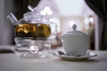 Transparent glass teapot on candle heater and sugar bowl with teaspoon, focus on tip of teaspoon.