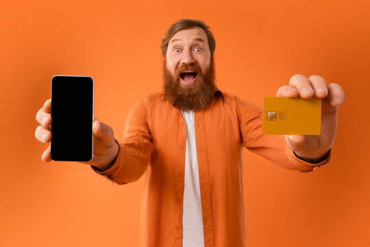 gingerhead bearded man showing blank smartphone and credit card, studio