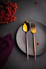 Cutlery for food, gold fork and spoon on a black plate, on a dark background. Table setting