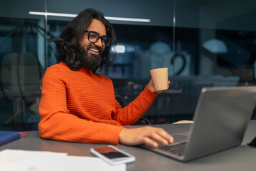 Man holding cup while working on laptop