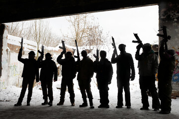 Eight unrecognizable young people with guns pose during lasertag game outdoor at winter day
