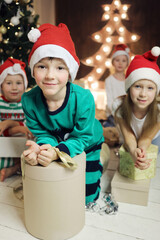 Two little boys, two girls with gifts in boxes are in room with christmas tree, focus on boy in green