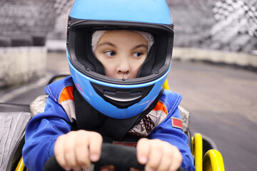 Little funny boy in helmet drives in go-kart on track during competition - obrazy, fototapety, plakaty