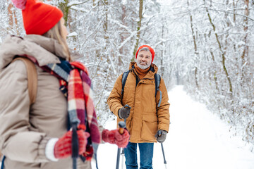 Mature couple having a walk in a snowy forest with scandinavian sticks