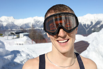 Half-naked skier in ski goggles smiles on mountain in ski resort at winter day