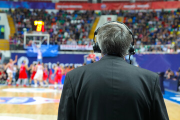 Commentator in headphones and suit at basketball game, back view