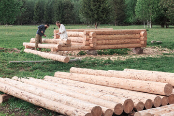 Two men are building a wooden house from logs in nature, logs in the foreground, construction, village, summer, greenery, forest, summer.
