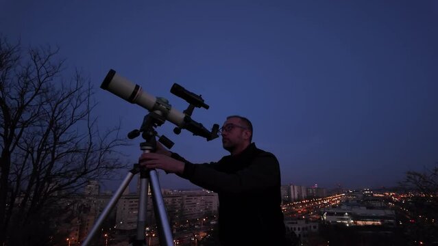 Amateur astronomer looking at the evening skies, observing planets, stars, Moon and other celestial objects with a telescope in urban city area.