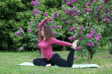 Woman practicing yoga on rug near bushes of blossoming lilacs at spring day