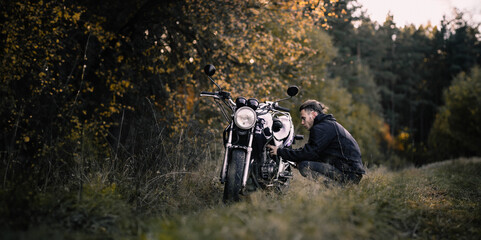male motorcyclist in nature with a custom classic motorcycle. Stylish male biker
