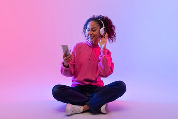 Smiling black lady with headphones using smartphone
