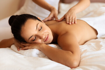 woman enjoying massage and calming touch of masseuse's hands indoor