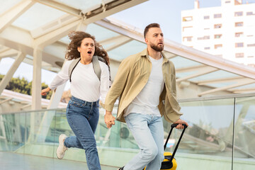 Stressed young couple running in airport terminal, late for their flight