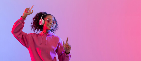 Woman in pink with headphones dancing under neon, free space