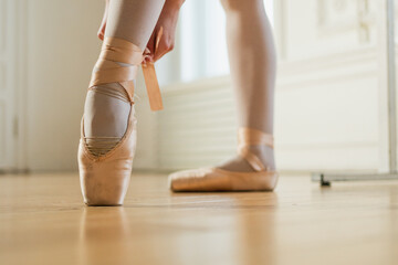 Ballerina puts on pointe shoes on leg in dance class. Classical ballet dancer woman in dance...