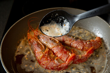 Cooking langoustine on frying pan with butter and garlic.