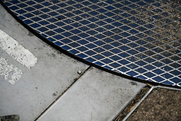 A close-up of a metallic grate against concrete, textures and patterns juxtaposed.