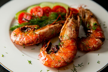 Cooked langoustine served on plate with cherry tomatoes and greens. Hand squeezing lemon juice on top.