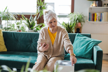 Senior woman using smartphone to set up a home air purifier
